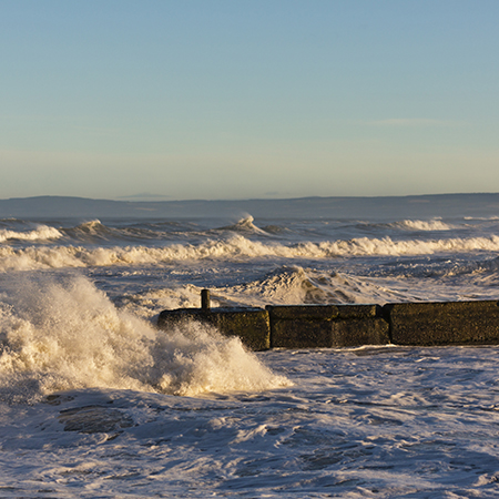 Waves crash along a barricade by the shore