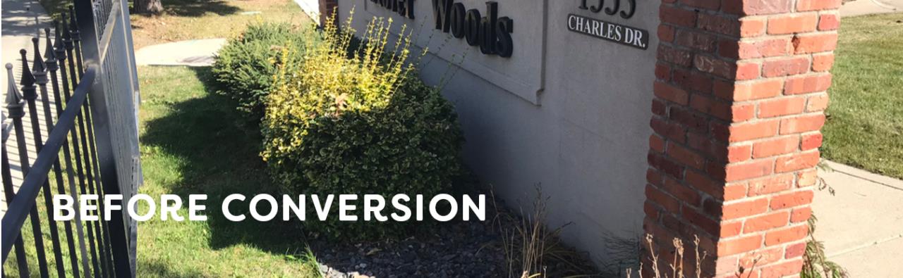 Shrubs and poorly maintained grass is seen in front of the Hover Woods neighborhood entry sign