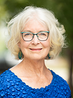 Joan Peck, an older white woman wearing a blue blouse and glasses, sits for a portrait for Longmont Mayor