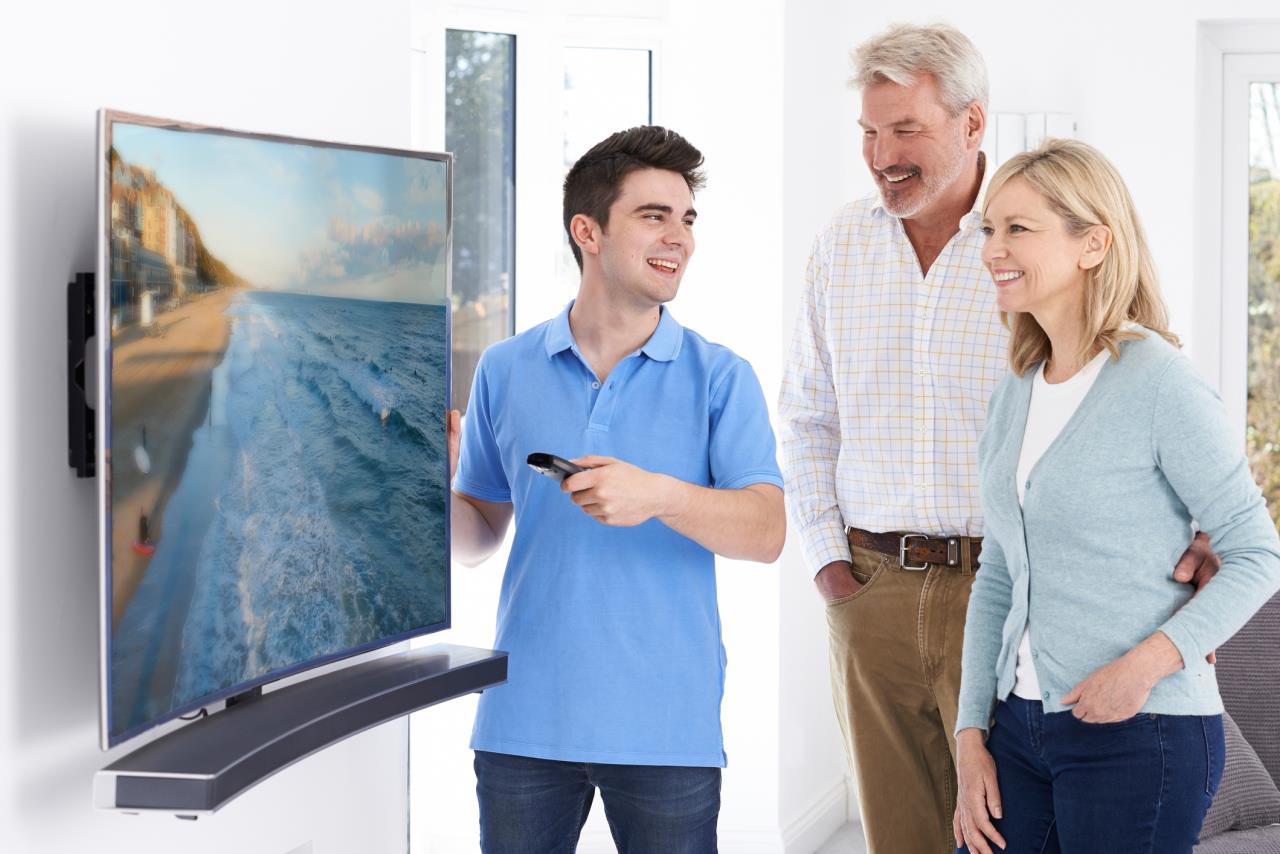 Young man helping older couple with modern TV