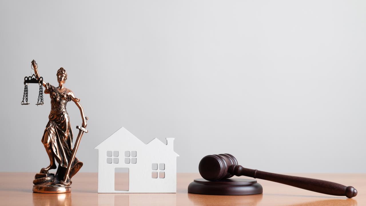 The scales of justice and a gavel appear next to a model of a home