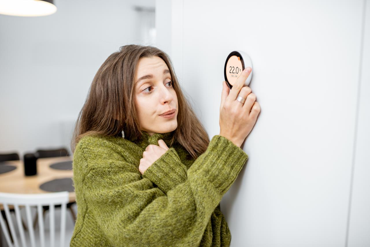 Cold woman in sweater adjusting smart thermostat