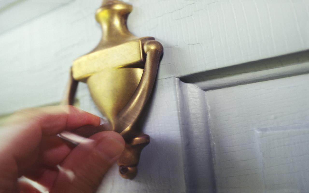 Hand using brass door knocker on white door