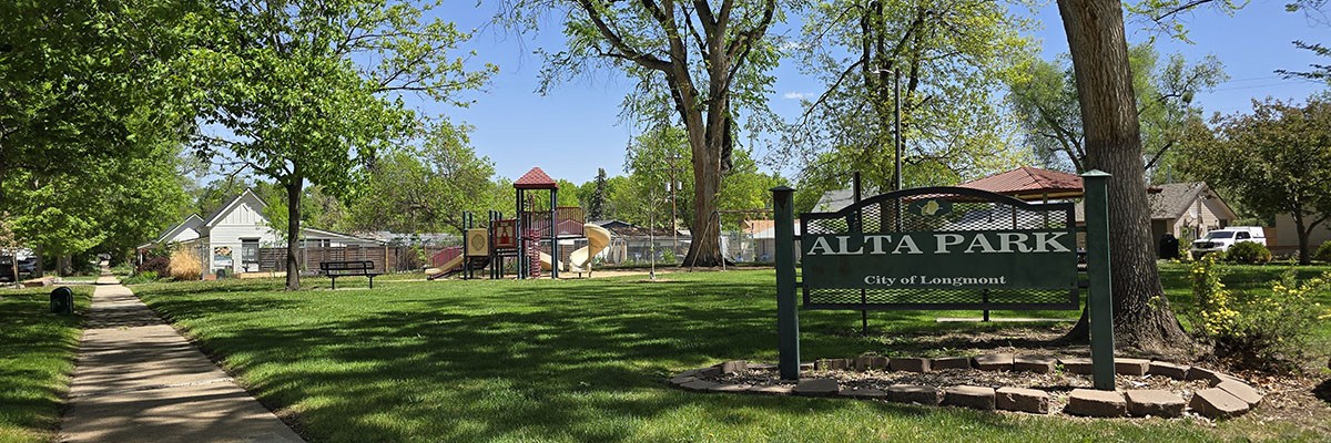Alta Neighborhood Park, and a sign with its name on it, are seen in a wooded area with green grass.