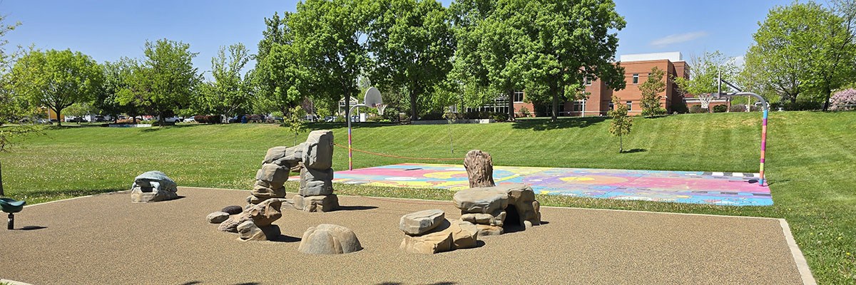 Athletic Field Neighborhood Park is viewed on a sunny summer day; there are rock sculptures in the foreground and a colorfully-painted basketball court in the background.