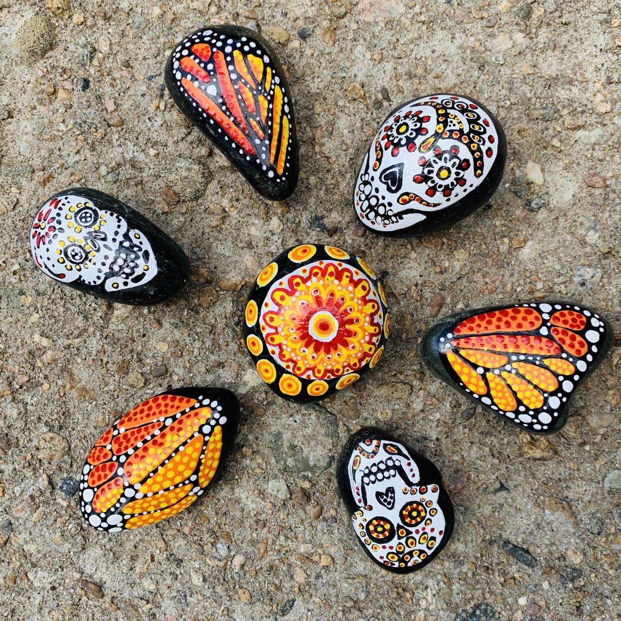 Day of the Dead stones depicting sugar skulls, monarch butterfly wings and marigold flowers.