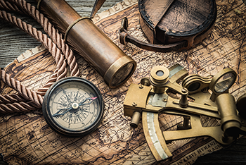 An antique map has vintage items on it including a compass, sextant, and telescope