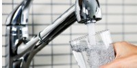 Glass of tap water being filled from stainless faucet