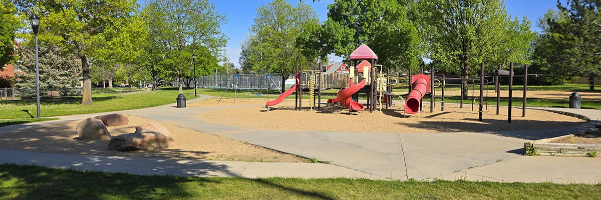 A colorful play structure is set against green trees and blue skies at Garden Acres Community Park.