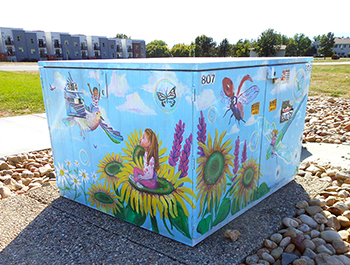 Painted on a power box: Happy children sit on flowers and fly on birds and bees under a pretty blue sky