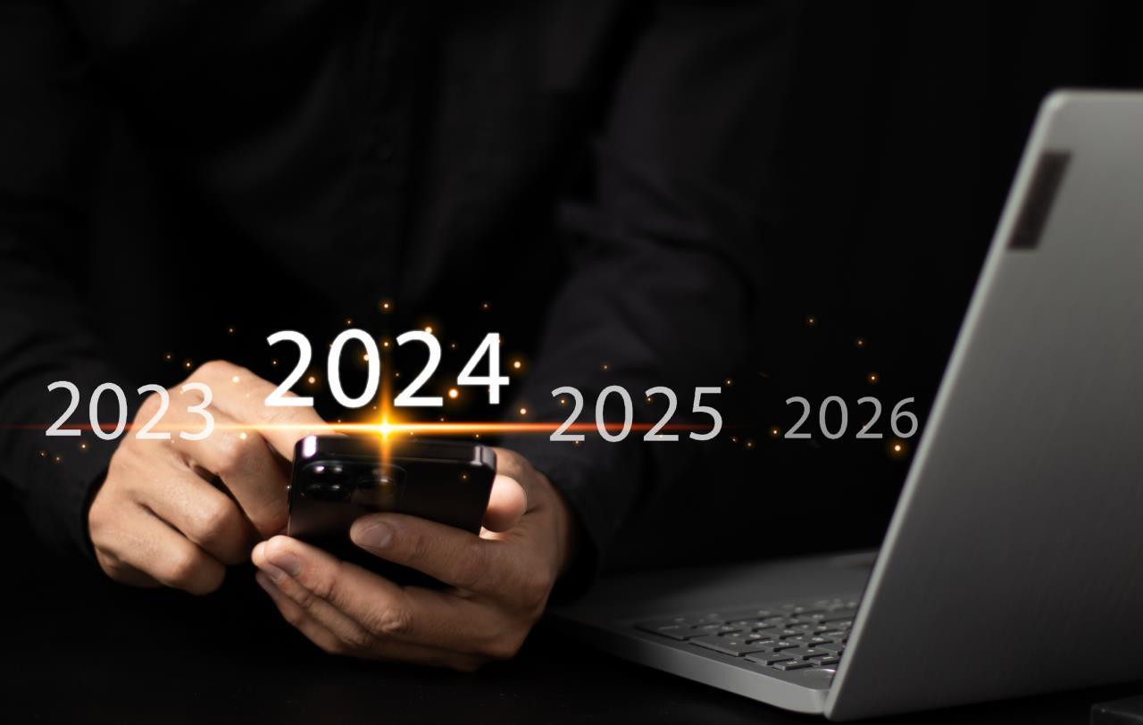 Hands selecting 2024 on smartphone near laptop