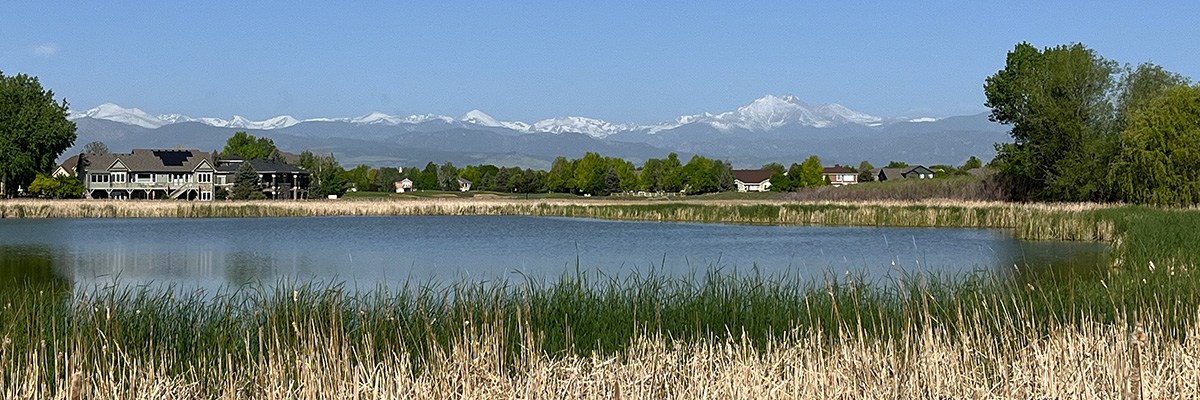 The pond at Jim Hamm Nature Area is seen with mountains and blue sky in the background.