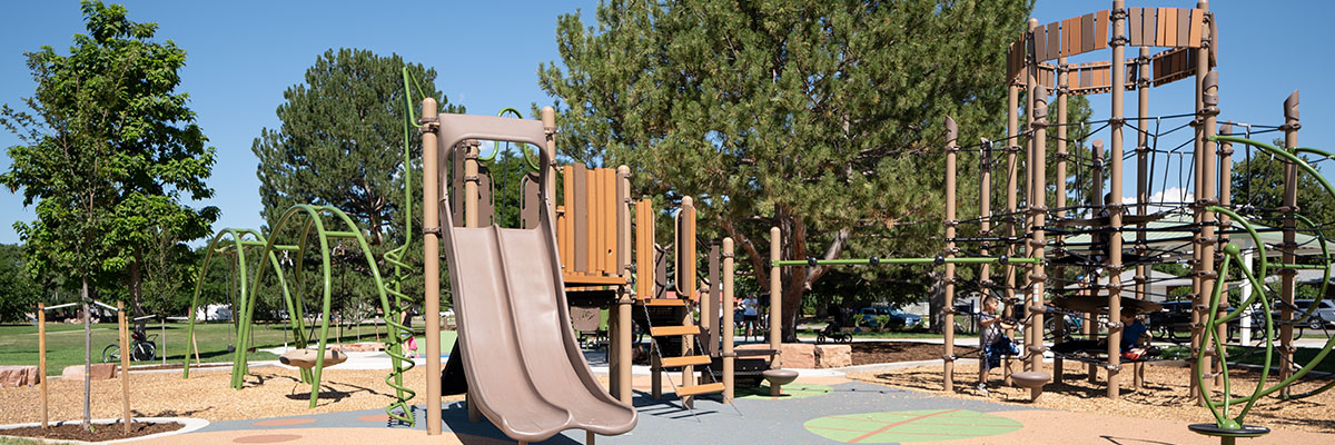 A new, brightly colored play structure is surrounded by green trees at Loomiller Neighborhood Park.