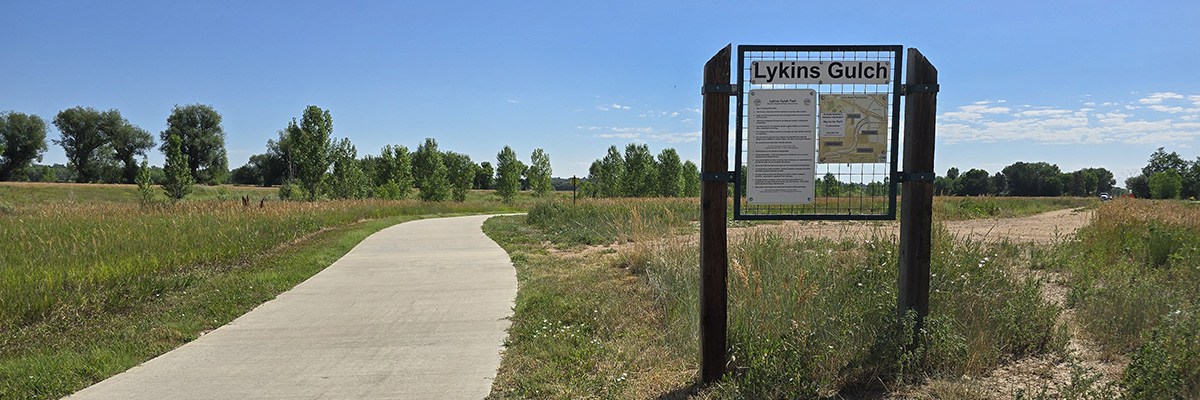 A "Lykins Gultch" sign appears alongside a sidewalk cutting through a green field.