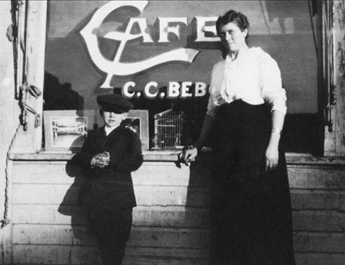 A historic photo of a boy with a woman standing in front of a store