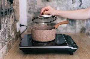 Pot being heated on portable induction cooktop as woman's hand lifts lid