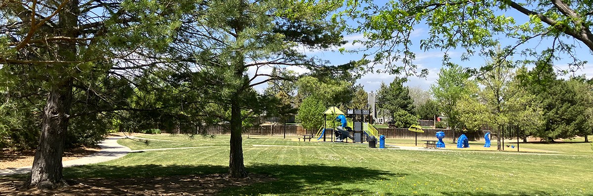 Raber Park is pictured in the late spring, with green grass and green trees framing a distant playground.