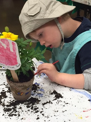 boy in hat painting flower pot