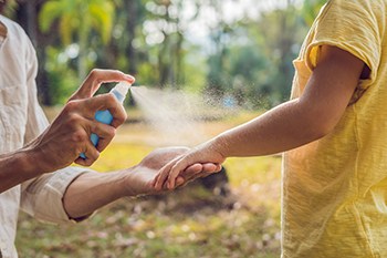 An adult sprays bug spray on a child's arm