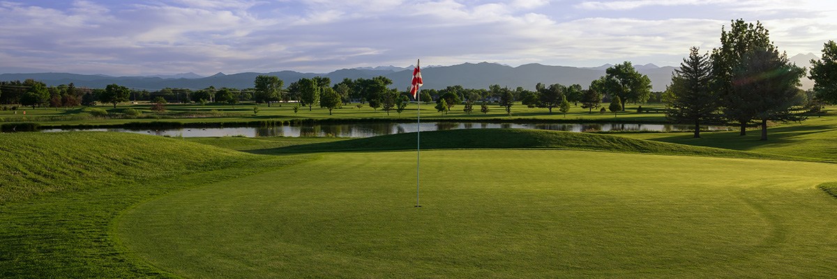 A green on the Twin Peaks Golf Course is in the foreground with the Rocky Mountains in the background.