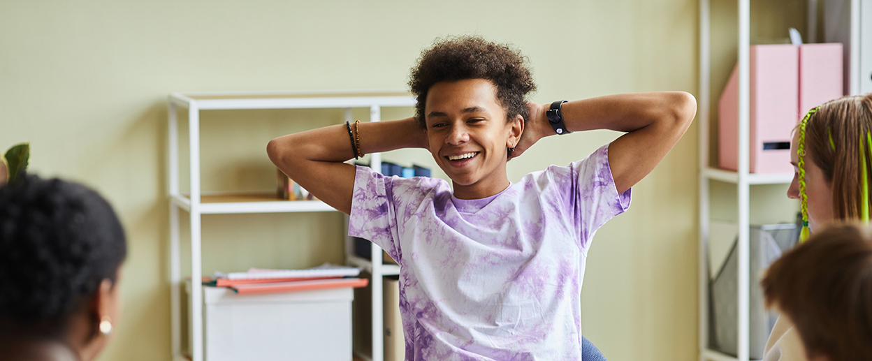 African teenage boy sitting on chair and smiling, he behaving badly during psychological session with group and psychologist