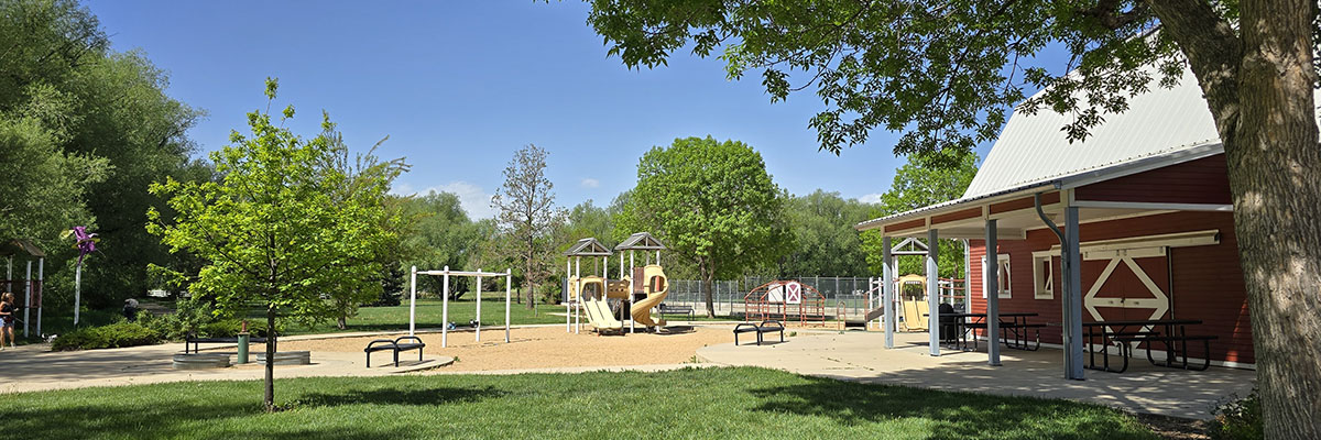 A a building wresembling a classic red barn provides a shaded area next to a playground.