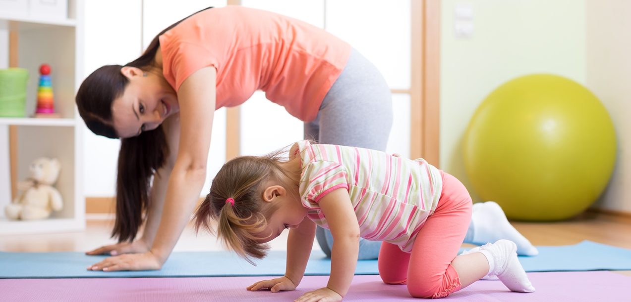 Mother and child daughter practicing yoga together in living room at home. Sport and family concept.