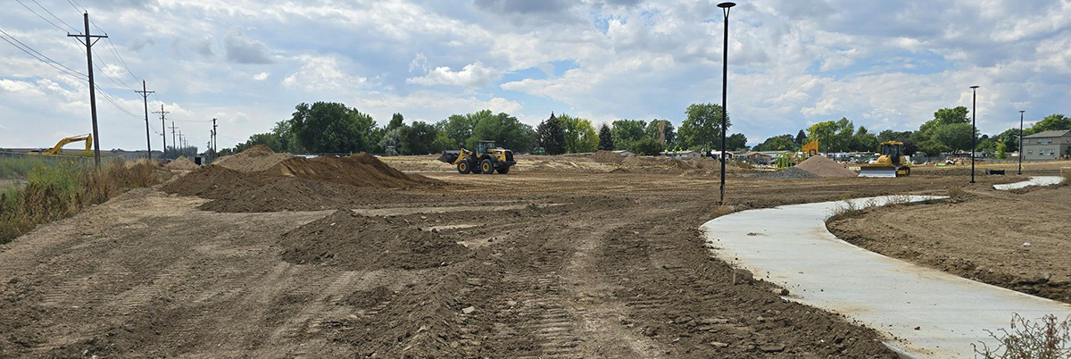 The Nino Gallo park is shown under construction, with a paved bike path passing through a field of dirt, with dirt moving machines in the background.