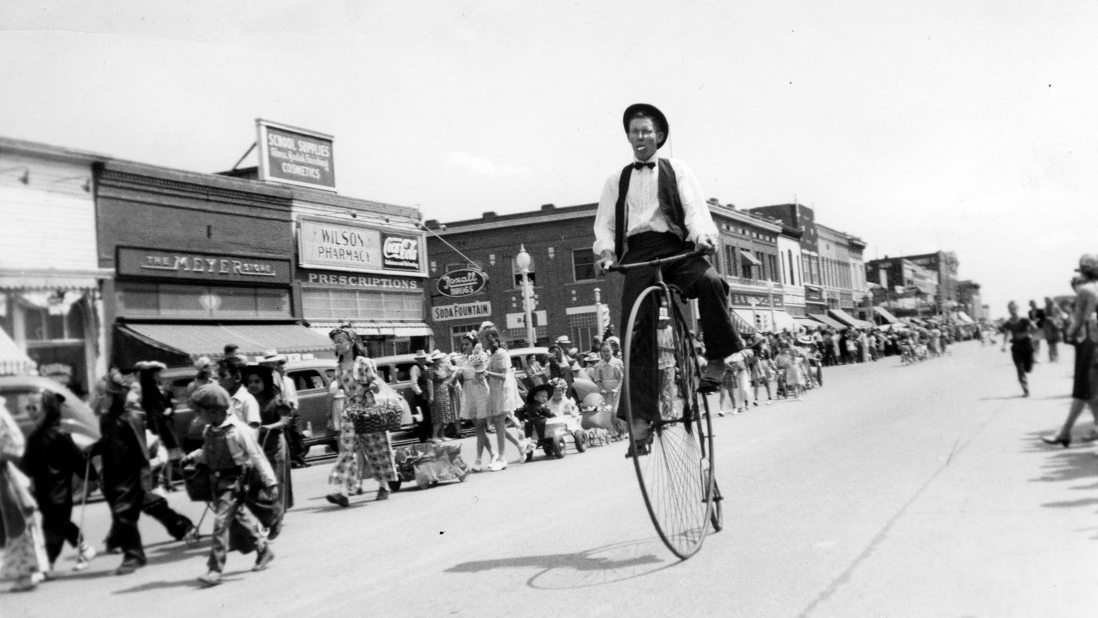 black and white image of man riding a penny farthing bicycle