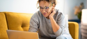 Female sitting on a yellow couch using laptop and internet connection and smiling