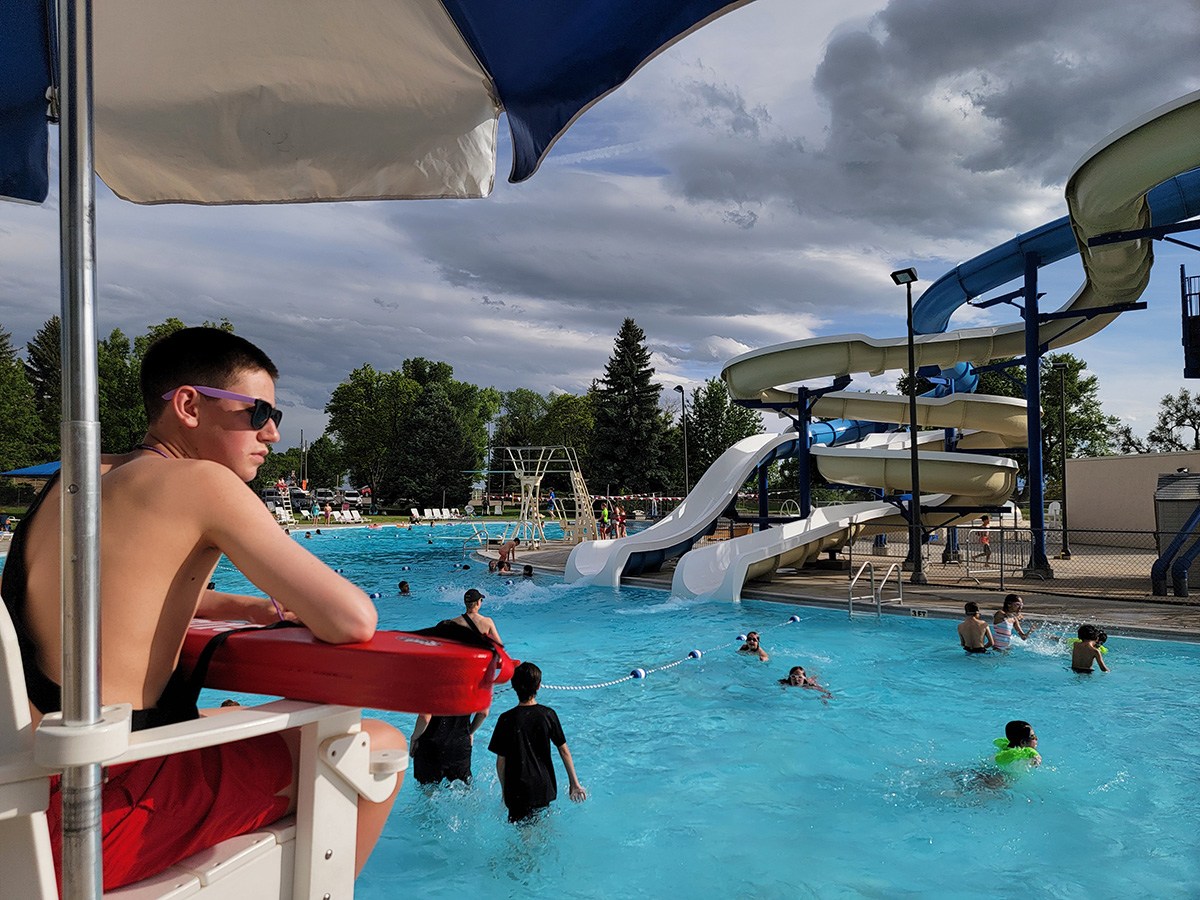 Lifeguard in foreground watching swimmers at Sunset Pool with slides in the background