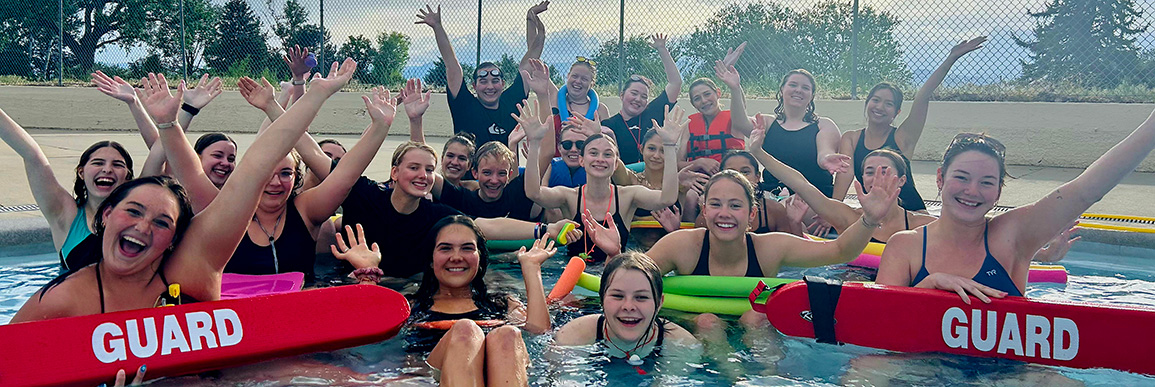 Group of lifeguards in the pool smiling and raising their hands.