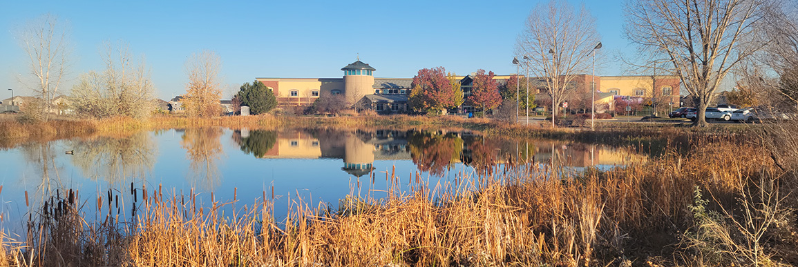 View of Longmont Recreation Center in the fall from across the pond. A reflection of the building is in the water.