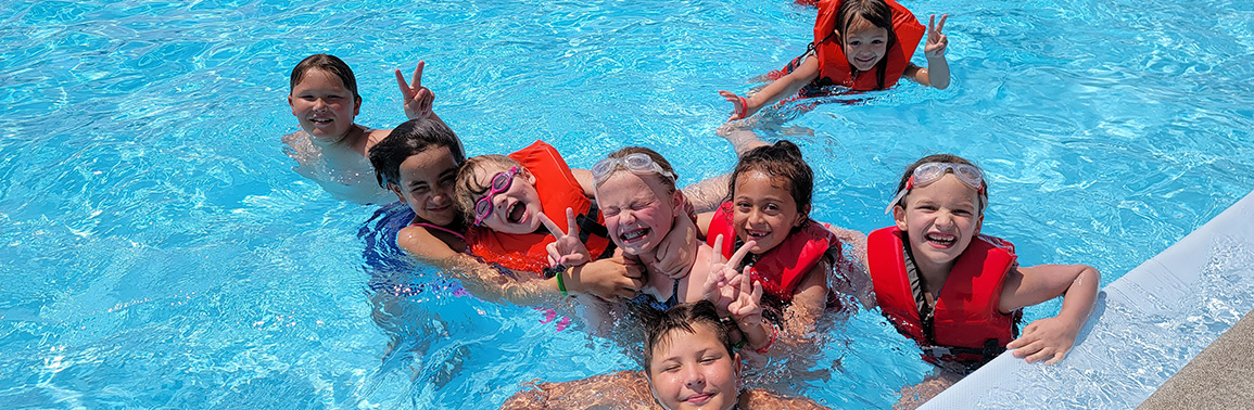 Smiling youth in life jackets pause their swimming at Sunset Pool for a photo.