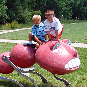 two young children on top of a red ant sculpture in a park