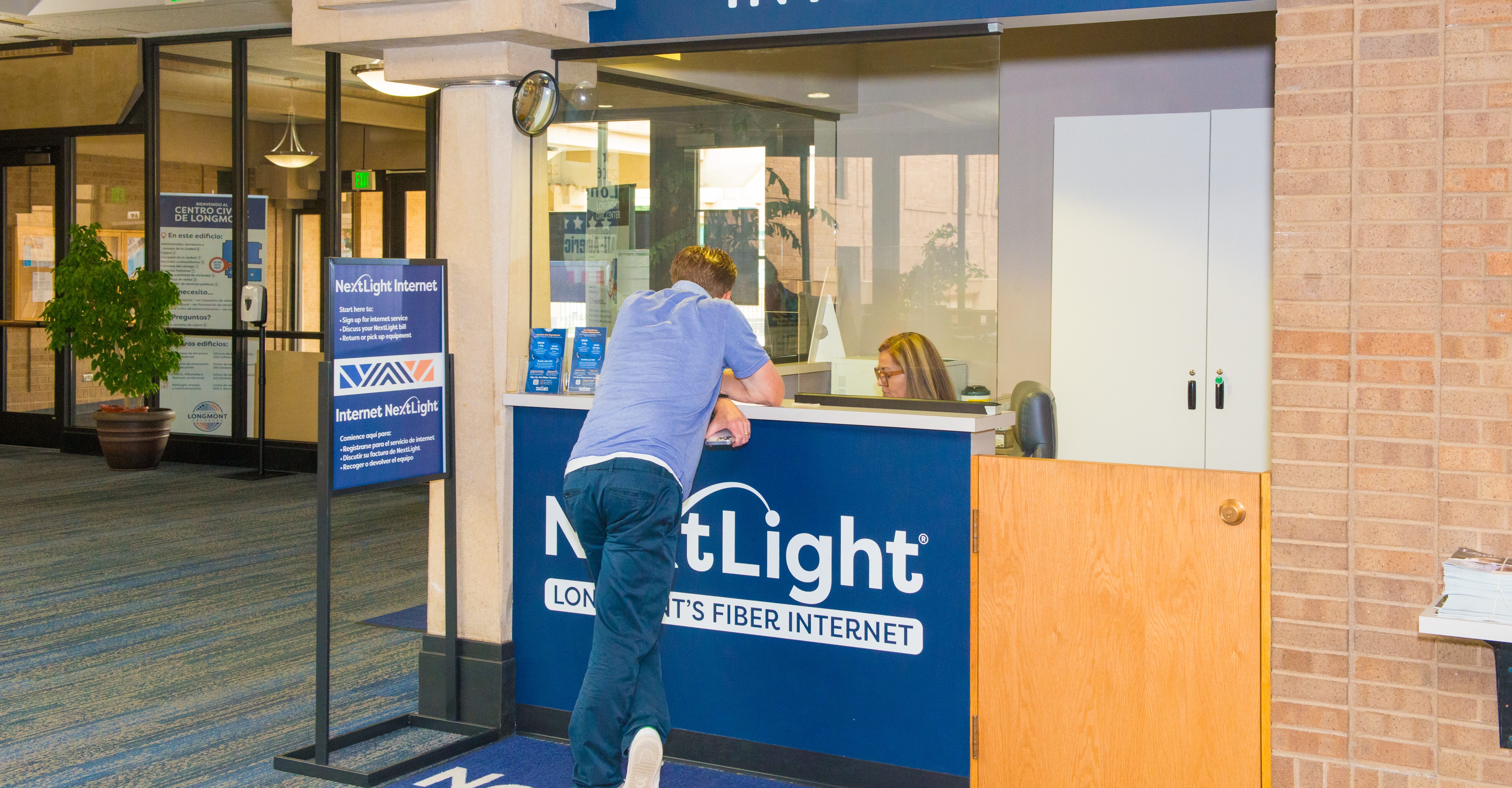 NextLight service desk in the Longmont Civic Center. Man leans against the counter as he is helped.