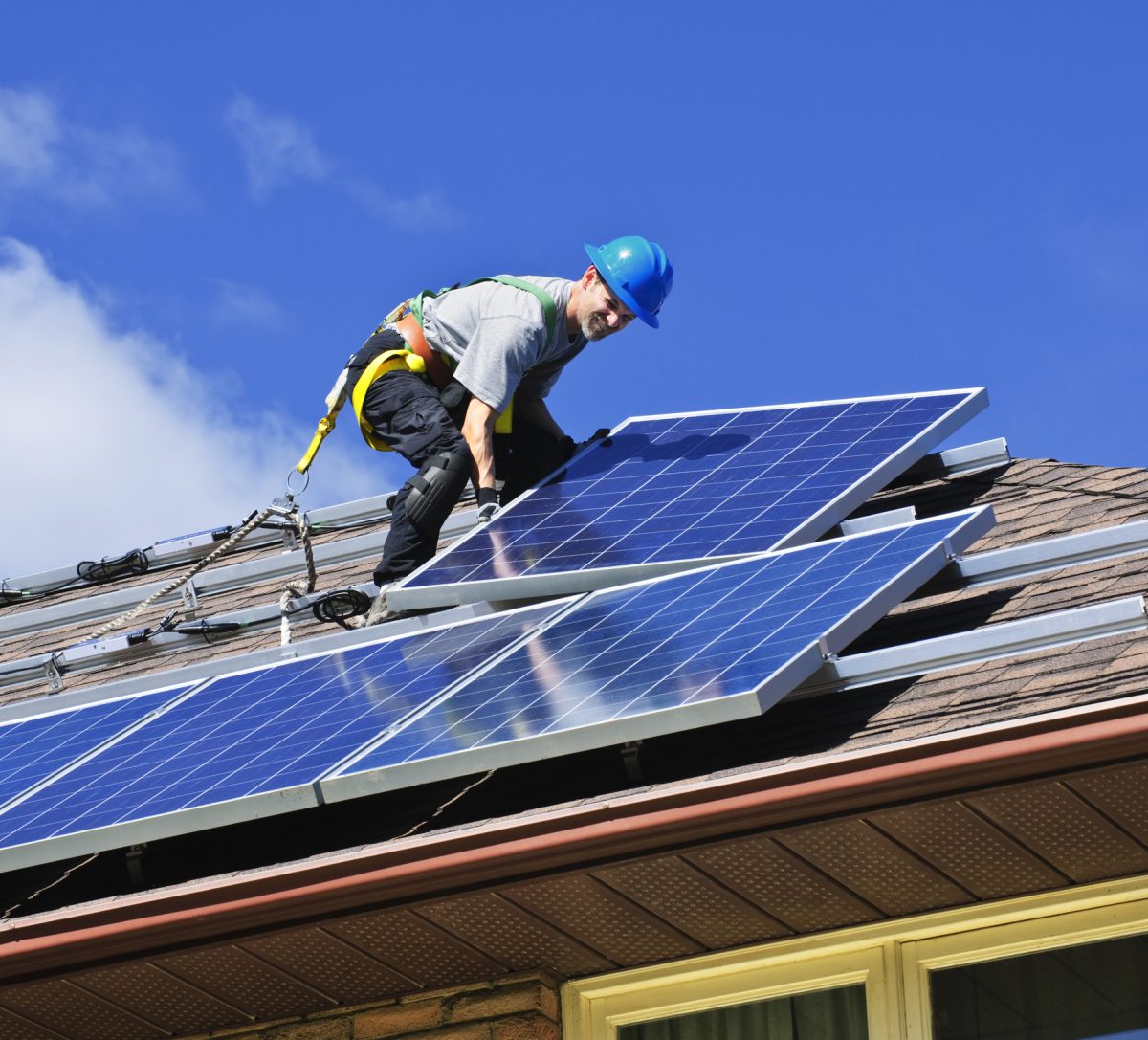 Man installing solar panels on roof of house