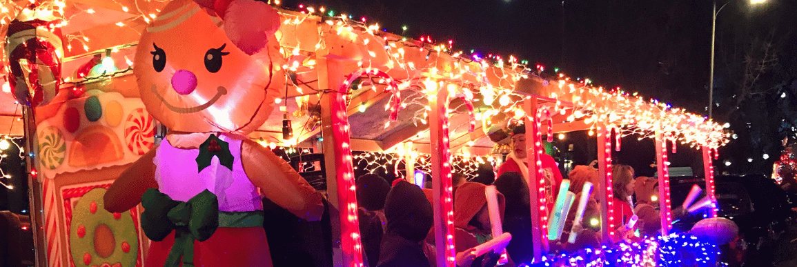 decorated holiday parade float with lights and inflatable gingerbread with kids singing