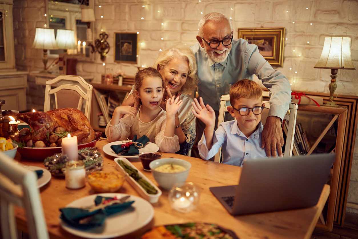 Older adults and children at Thanksgiving table waving to a laptop for a video call.