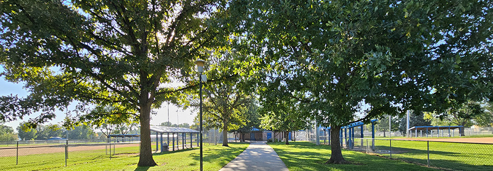 A sidewalk passes beneath several leafy trees at Garden Acres park.