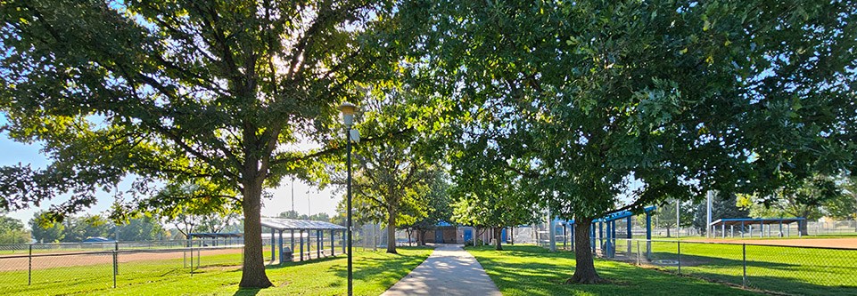 A sidewalk passes beneath several leafy trees at Garden Acres park.