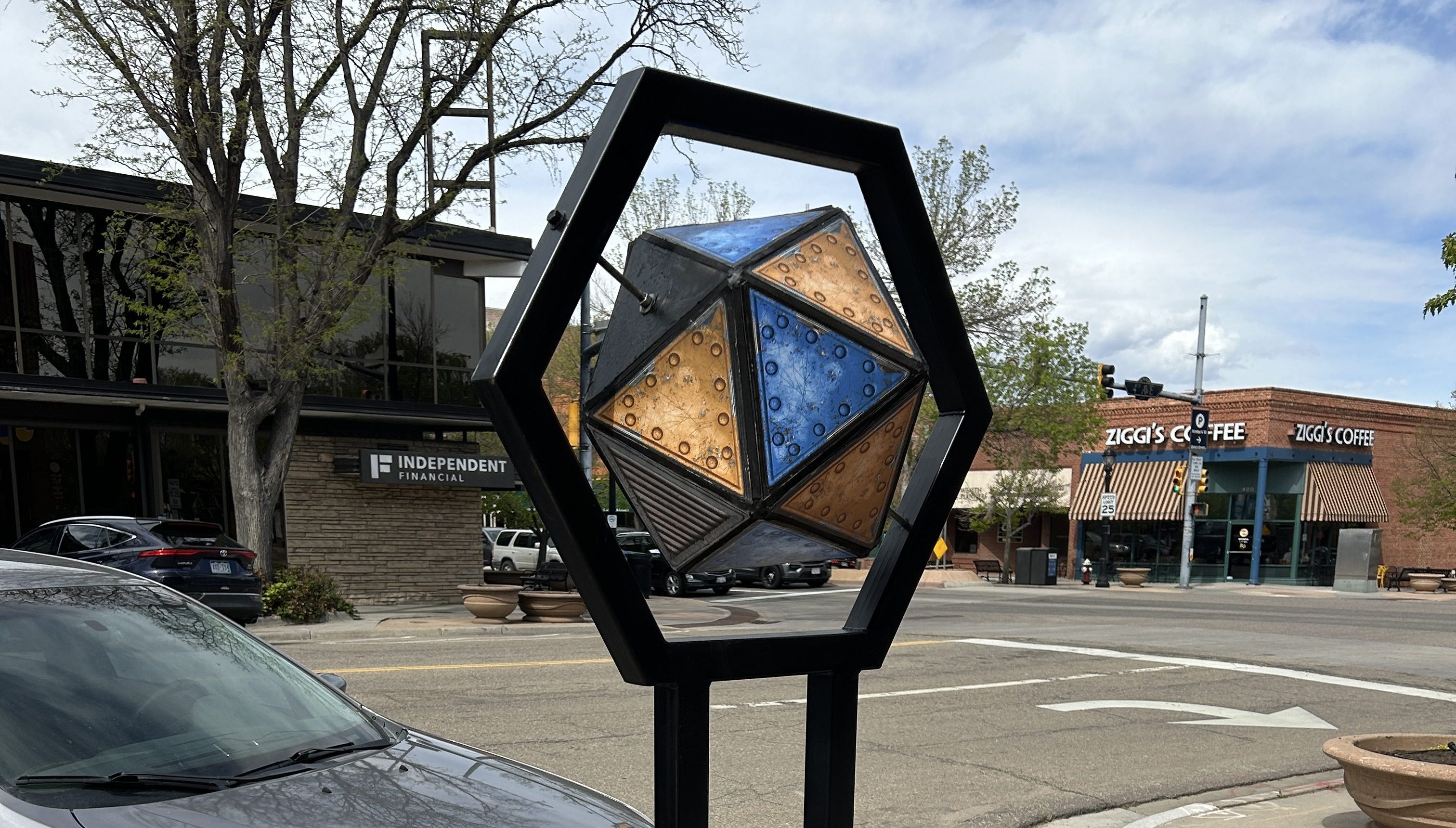 a sculpture with a multisided shape with a black metal armature on the sidewalk