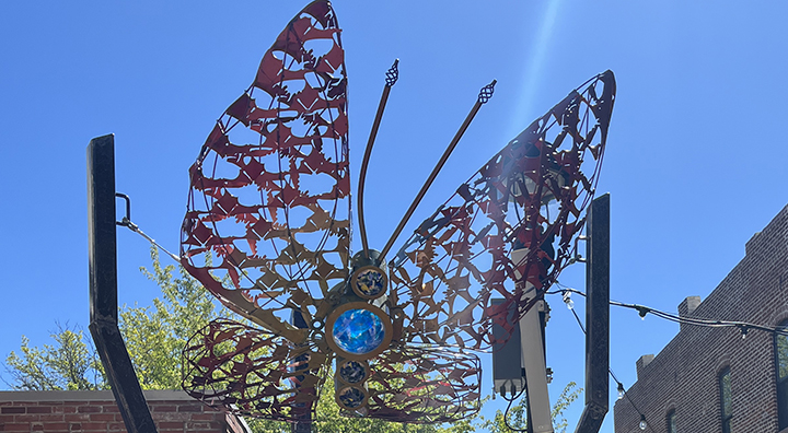 a close up an oversized butterfly, suspended between black posts and a blue clear sky in the background