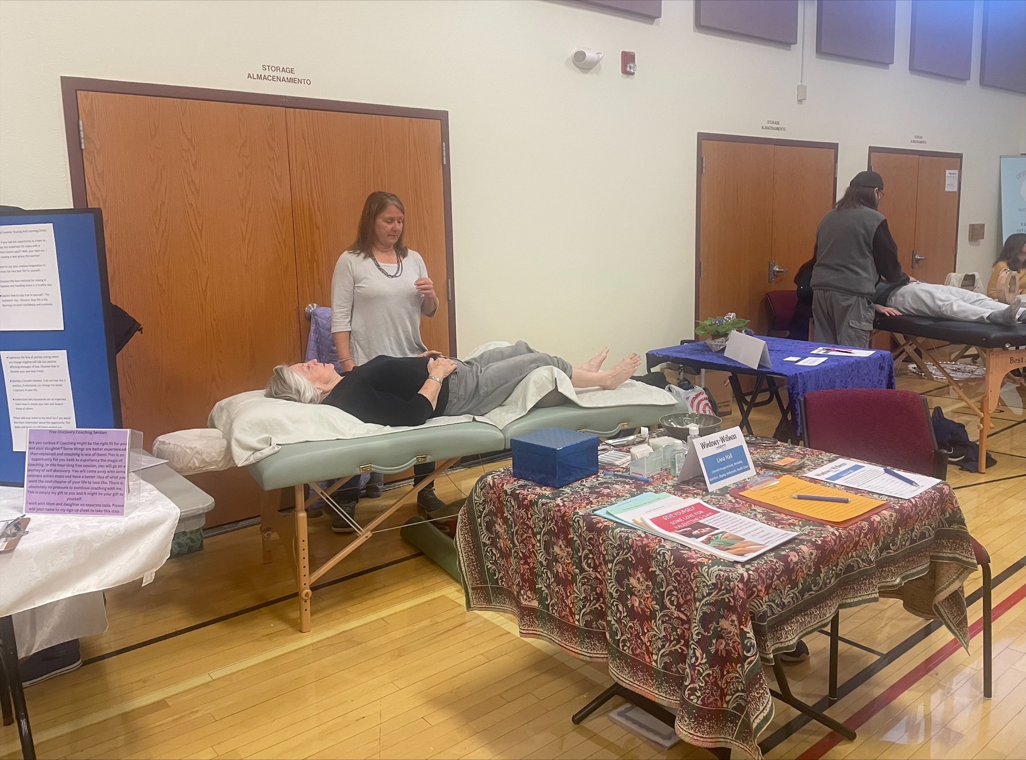 Image of a past Windows to Wellness event held in a gymnasium with an attendee laying on a massage table and a care provider standing next to them.