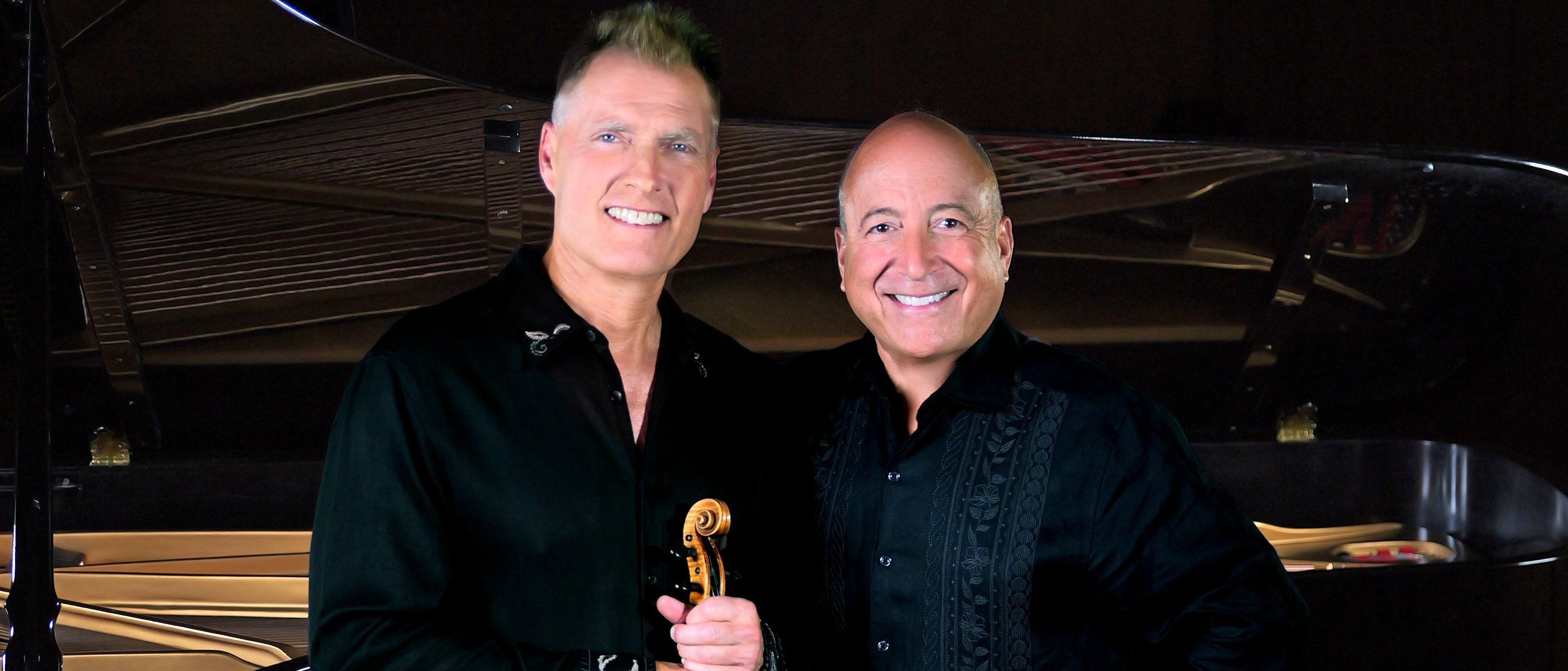 Two men in black one holding a violin against a dark background