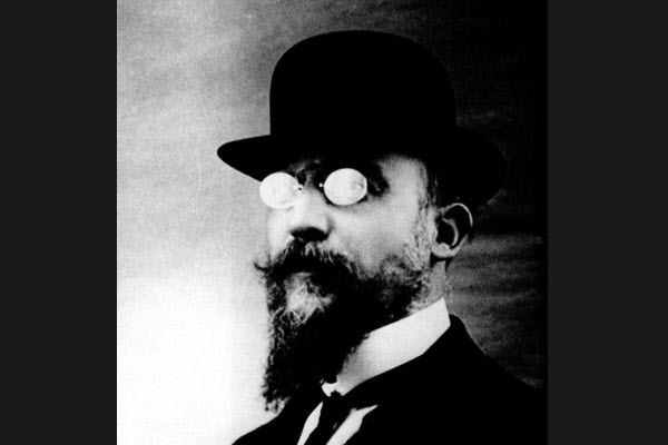 Black and white image of Erik Satie with glasses, beard, and hat