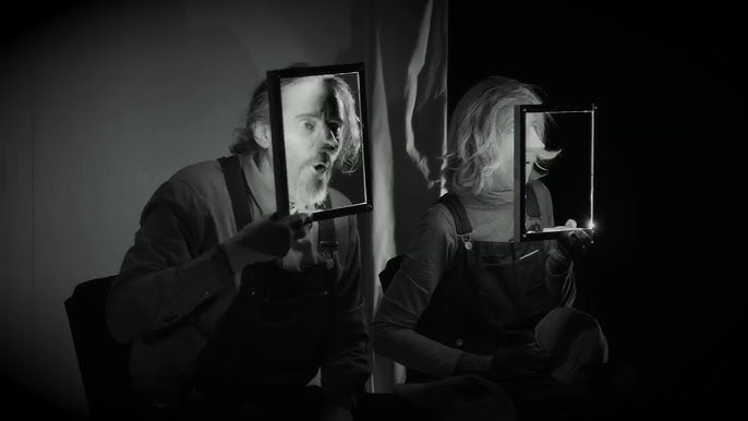 Black and white film-style still of Betsy Tobin holding a frame in front of their face