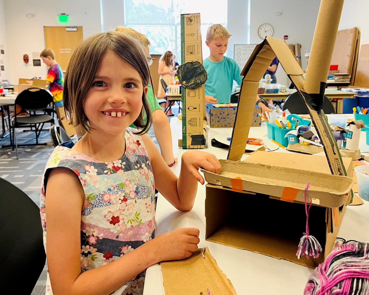 A girl sitting at a table with a creation made from carboard