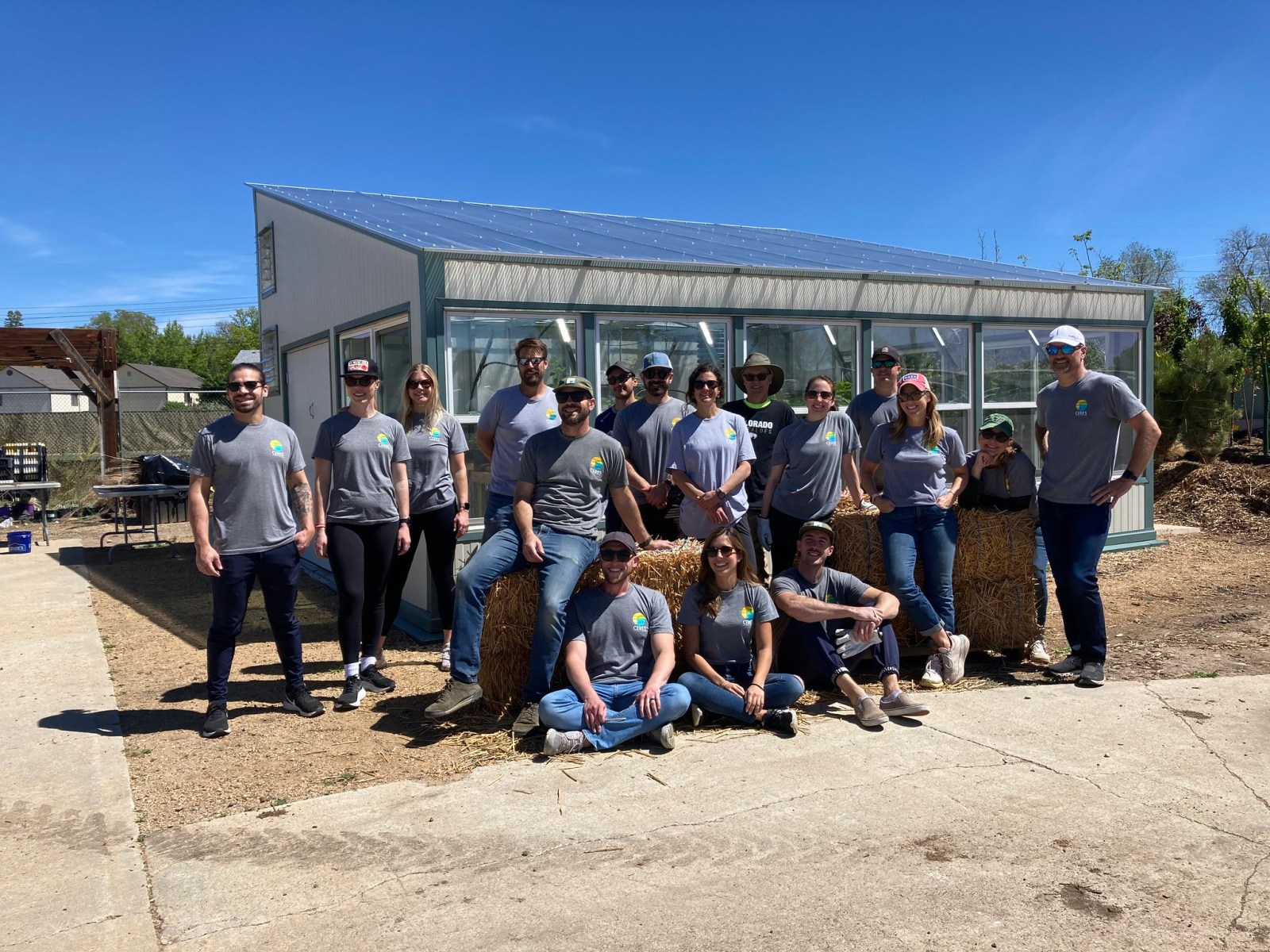 A group of people all wearing gray shirts standing in front of a greenhouse