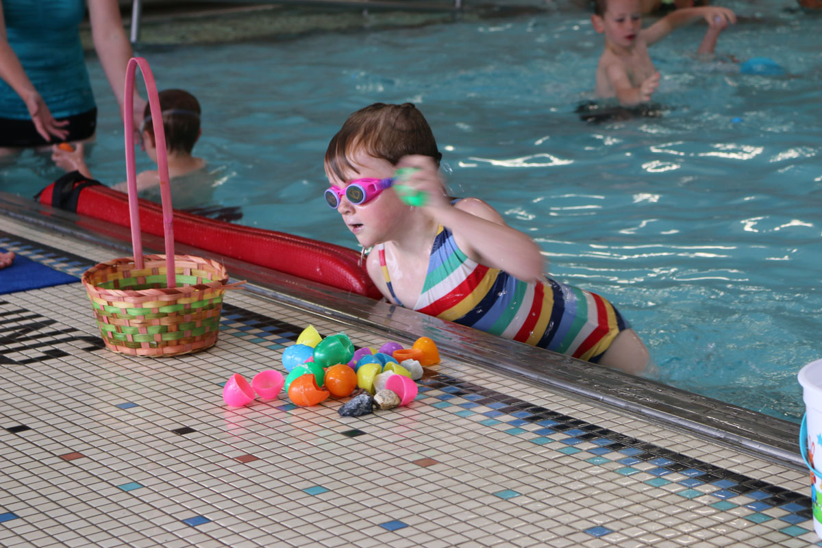 Girl in striped bathing suit with goggles hunting Easter eggs in pool